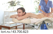 Focused professional mature masseuse performing anti-cellulite thigh massage to young female client in spa center. Стоковое видео, видеограф Яков Филимонов / Фотобанк Лори