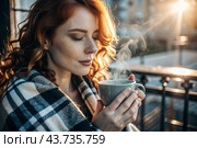 A red-haired, beautiful woman wrapped in a plaid with a mug of hot coffee on a beautiful patio in the rays of the setting sun. The girl inhales the aroma of the drink. Comfort and harmony. Стоковое AI-изображение, AI-художник Photojuli / Фотобанк Лори