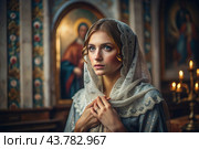 Portrait of a beautiful young woman in a headscarf in an Orthodox church. A girl prays in a church against the background of icons. Стоковое AI-изображение, AI-художник Photojuli / Фотобанк Лори