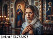 Portrait of a beautiful young woman in a headscarf in an Orthodox church. A girl prays in a church against the background of icons. Стоковое AI-изображение, AI-художник Photojuli / Фотобанк Лори