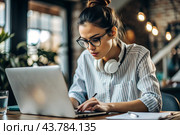 A young female freelance businessman in glasses and headphones is working on a laptop or shopping in an online store. The woman is writing something in a notebook. Стоковое AI-изображение, AI-художник Photojuli / Фотобанк Лори