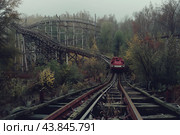 Red rollercoaster cart approaching on tracks in abandoned amusement park on foggy day. Стоковое AI-изображение, AI-художник Иван Рябоконь / Фотобанк Лори