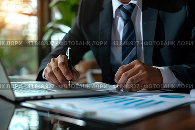 Businessman analyzing financial documents and using laptop in office. Стоковое AI-изображение, AI-художник Иван Рябоконь / Фотобанк Лори