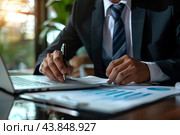 Businessman analyzing financial documents and using laptop in office. Стоковое AI-изображение, AI-художник Иван Рябоконь / Фотобанк Лори