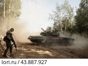 Выстрел танка русского танка Т-80 на лесной дороге поднял пыль и военный с автоматом (2018 год). Редакционное фото, фотограф Евгений Зимин / Фотобанк Лори