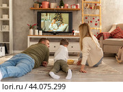 Happy family eating popcorn on a floor in front of TV. Smiling laughing parent showing funny video to son on television. Parent and son watching comedy movie on tv-set at home. Стоковое фото, фотограф Ирина Михайличенко / Фотобанк Лори