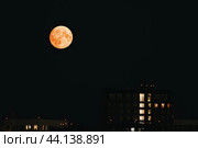 Dark night with a full moon hanging high above the urban landscape of buildings. Стоковое фото, фотограф Константин Григорьев / Фотобанк Лори