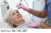 Delighted old woman lying on clinical chair in aesthetic cabinet during face RF-lifting procedure. Стоковое видео, видеограф Яков Филимонов / Фотобанк Лори