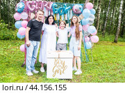 Семья с двумя детьми на вечеринке по определению пола "Гендер пати" в парке. Мама, папа, сын и дочь стоят перед коробкой с надписью «мальчик или девочка», в которой содержится ответ на вопрос, кто родится. Стоковое фото, фотограф Яна Проничева / Фотобанк Лори