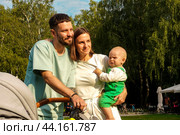 Молодая семья держит на руках свою маленькую дочь во время пикника в парке. Стоковое фото, фотограф Ярославский Максим / Фотобанк Лори
