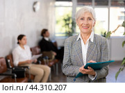 Smiling secretary senior woman stands at entrance to office reception and expects visitors. Стоковое фото, фотограф Яков Филимонов / Фотобанк Лори