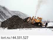 Бульдозер в горной местности сгребает кучу горного золотосодержащего грунта , который в дальнейшем будет перевозиться на промывку с целью извлечения желтого драгоценного метала. Стоковое фото, фотограф Павел Просянов / Фотобанк Лори