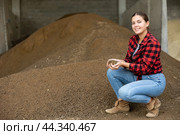 Young dairy farm female worker squatting at heap of soybean husk in fodder storage. Стоковое фото, фотограф Яков Филимонов / Фотобанк Лори