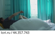 A man wakes up in bed in the morning, sitting on the bed and stretching. Стоковое видео, видеограф Ярославский Максим / Фотобанк Лори