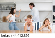 Two children sitting at the kitchen table sadly while their parents quarrelling. Стоковое фото, фотограф Яков Филимонов / Фотобанк Лори