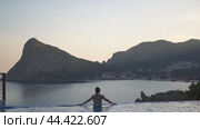 A woman is sitting in a pool with a beautiful view of the ocean. The water is calm and the sky is clear. Стоковое видео, видеограф svetograph / Фотобанк Лори