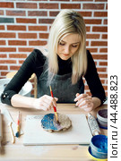 Woman making pattern on ceramic plate with paint brush. Creative hobby concept. Earn extra money, side hustle, turning hobbies into cash, passion into job, vertical. Стоковое фото, фотограф Natalia Gdovskaia / Фотобанк Лори