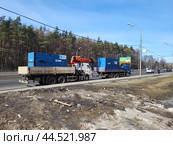 Two cargo trucks carrying blue industrial generators branded "SDMO" and "MSK energo" with a red crane parked on a roadside near a forest - Moscow, Russia, March 20, 2023. Редакционное фото, фотограф Андрей Журавлев / Фотобанк Лори