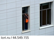 Рабочий на стройке прикручивает крепёж для москитной сетки на окне (2024 год). Редакционное фото, фотограф MК / Фотобанк Лори