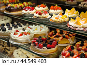 Assorted fresh fruit tarts and cakes in bakery display. Стоковое AI-изображение, AI-художник Иван Рябоконь / Фотобанк Лори