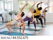 Young woman coach and students perform utkata konasana during training in studio. Стоковое фото, фотограф Яков Филимонов / Фотобанк Лори