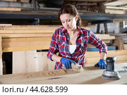 During manufacturing, woman employee grinds surface of wooden board, gives smoothness to surface. Стоковое фото, фотограф Яков Филимонов / Фотобанк Лори