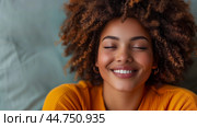 Smiling woman with curly hair and closed eyes wearing a  yellow sweater, radiating calmness and happiness. Стоковое AI-изображение, AI-художник Anastacia Gaikova / Фотобанк Лори
