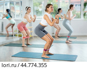 Young woman during Pilates strength training performs squats with elastic band on legs and shins. Стоковое фото, фотограф Яков Филимонов / Фотобанк Лори