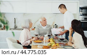 Young guy giving present to old man while sitting around kitchen table full of snacks and red wine. Стоковое видео, видеограф Яков Филимонов / Фотобанк Лори