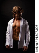 Sporty man in unbuttoned white shirt with abs muscle press posing in shadow at black, studio shot. Portrait of handsome guy with perfect muscular sexy torso, advertising model pose. Copy ad text space. Стоковое фото, фотограф Aleksandr Golubev / Фотобанк Лори