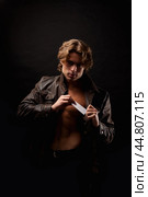 Perfect young man in unbuttoned image leather jacket showing visit card posing in black studio shadow, looking at camera. Handsome guy fashion model with lovely muscular sexy torso. Copy ad text space. Стоковое фото, фотограф Aleksandr Golubev / Фотобанк Лори
