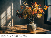 Branches with golden autumn leaves in a ceramic vase on a wooden table by the window. The concept of home comfort. Autumn decor for Halloween. Стоковое AI-изображение, AI-художник Photojuli / Фотобанк Лори