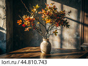 Branches with golden autumn leaves in a ceramic vase on a wooden table by the window. The concept of home comfort. Autumn decor for Halloween. Стоковое AI-изображение, AI-художник Photojuli / Фотобанк Лори