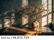 Branches with golden autumn leaves in a ceramic vase on a wooden table by the window. The concept of home comfort. Autumn decor for Halloween. Стоковое AI-изображение, AI-художник Photojuli / Фотобанк Лори
