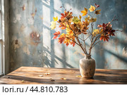 Branches with golden autumn leaves in a ceramic vase on a wooden table by the window. The concept of home comfort. Autumn decor for Halloween. Стоковое AI-изображение, AI-художник Photojuli / Фотобанк Лори