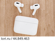 Closeup white TWS true wireless stereo earbuds and case on wooden table background. Closeup modern headphone. Стоковое фото, фотограф Павел Муравьев / Фотобанк Лори