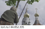 A woman stands under a chestnut tree and looks at the church женщина стоит под каштаном и смотрит на церковь. Стоковое видео, видеограф Опока Алексей / Фотобанк Лори