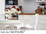 Still-life. White and red dahlia flowers in a vase, a teapot, a pumpkin and a house on a white table in the interior of a home kitchen. A cozy autumn concept. Стоковое фото, фотограф Photojuli / Фотобанк Лори