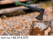An axe will be stuck into a wooden log. Harvesting firewood for the winter season. Logging on the background of a country house. Lumber, wood-cutting tools. Стоковое фото, фотограф Photojuli / Фотобанк Лори