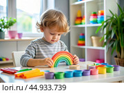 Toys. A little boy is playing educational games. A rainbow-shaped children's toy, colored pyramids and logic toys for children. Montessori games for child development. Стоковое AI-изображение, AI-художник Photojuli / Фотобанк Лори