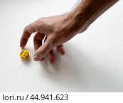 Hand reaching for yellow dice on white background symbolizing chance and decision-making. Стоковое фото, фотограф Lamina Akulova / Фотобанк Лори