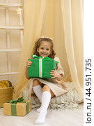 Christmas spirit. Happy little smiling girl is sitting in the children room in a tent and opening Christmas gifts. Happy girl unwrapping Christmas present box. Holidays and celebrations concept. Стоковое фото, фотограф Ирина Михайличенко / Фотобанк Лори