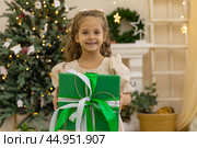 Christmas holidays. Happy little smiling girl holding box near the Christmas tree. Happy girl unwrapping Christmas present. Holidays and celebrations concept. Стоковое фото, фотограф Ирина Михайличенко / Фотобанк Лори