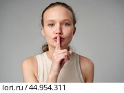Young Woman Making a Hush Gesture on gray background in studio. Стоковое фото, фотограф Сергей Толмачёв / Фотобанк Лори