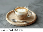 Cafe latte macchiato layered coffee in a see through coffee cup. Wooden tray with art milk coffee in a transparent trendy glass mug, spoon on gray desk. Hot cappuccino coffee on table. Space for text. Стоковое AI-изображение, AI-художник Марина Демидюк / Фотобанк Лори
