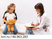 Mom bring her child, little daughter to the pediatrician office, register her and discuss with the doctor how to care for the children. Healthy lifestyle. The doctor fills out the health questionnaire. Стоковое фото, фотограф Ирина Михайличенко / Фотобанк Лори