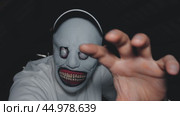 A man in a monster mask and white shirt holds out his hand. A black baseball cap is on his head. The monster lives in the attic. Стоковое видео, видеограф Воловодов Владимир / Фотобанк Лори