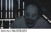A pale-faced creature with sunken eyes and a wide grinning mouth in a dark attic. Rays of light shine through boards, creating a stark contrast. The monster's ghastly grin inspires terror and fear. Стоковое видео, видеограф Воловодов Владимир / Фотобанк Лори