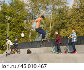 Moscow, Russia - September 5, 2019: Young skateboarder performs a trick on a city sports ground. Young man jumping over an obstacles. Children looking at his stunt and getting lesson. Extreme sports is very popular among youth. Side view. Редакционное фото, фотограф YuryKara / Фотобанк Лори