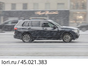 Автомобиль BMW X7 едет по улице во время снегопада. Черный внедорожник движется по заснеженной городской дороге. Редакционное фото, фотограф Константин Григорьев / Фотобанк Лори